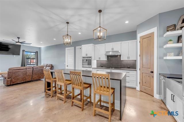 kitchen featuring tasteful backsplash, white cabinets, oven, hanging light fixtures, and a breakfast bar area