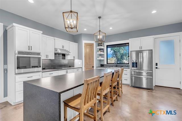 kitchen with appliances with stainless steel finishes, a kitchen breakfast bar, pendant lighting, white cabinets, and a kitchen island