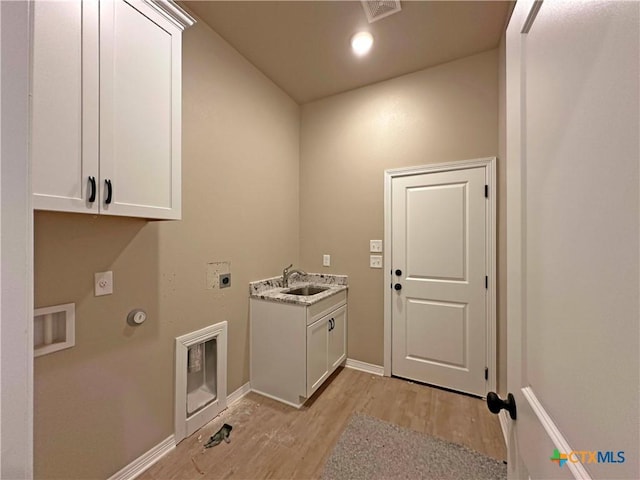 clothes washing area with sink, gas dryer hookup, cabinets, light wood-type flooring, and electric dryer hookup