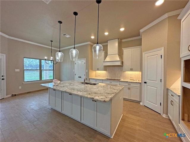 kitchen featuring premium range hood, sink, white cabinets, and an island with sink