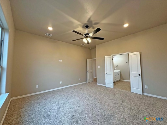 unfurnished bedroom featuring ceiling fan, light colored carpet, and ensuite bath