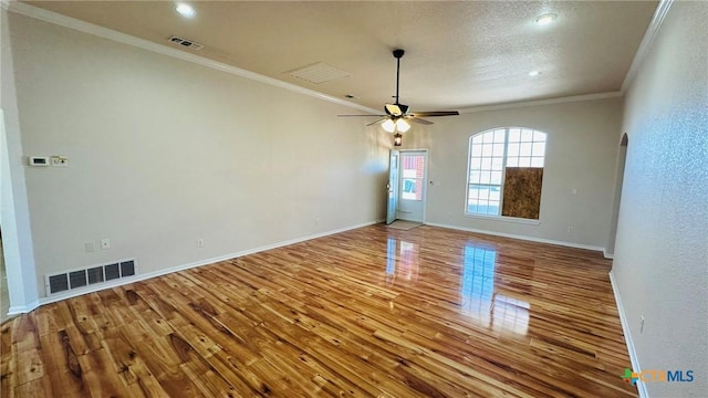 empty room with arched walkways, wood finished floors, visible vents, baseboards, and ornamental molding