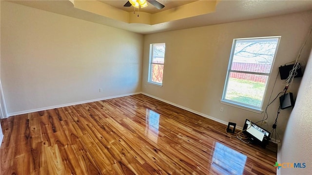 unfurnished room featuring a ceiling fan, baseboards, a raised ceiling, and wood finished floors