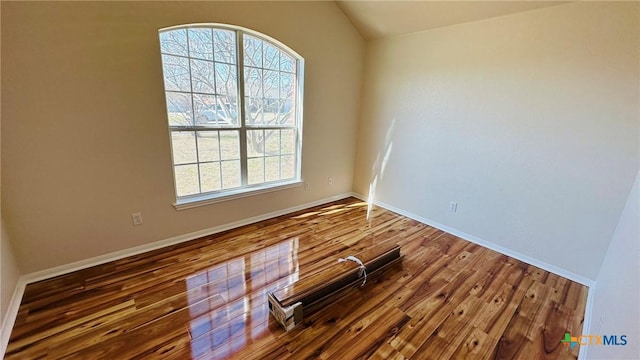 spare room featuring vaulted ceiling, dark wood finished floors, and baseboards