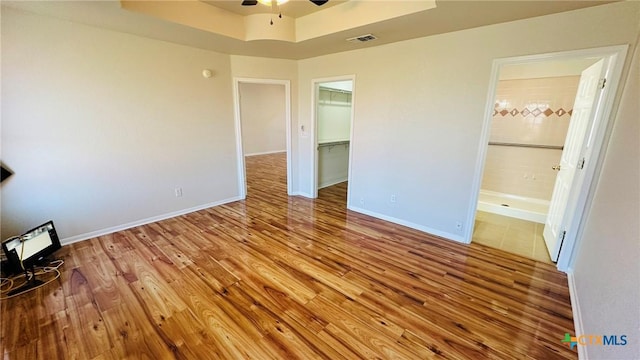 unfurnished bedroom with visible vents, baseboards, a ceiling fan, ensuite bath, and wood finished floors