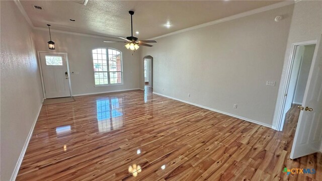 empty room featuring arched walkways, wood finished floors, a wealth of natural light, and baseboards