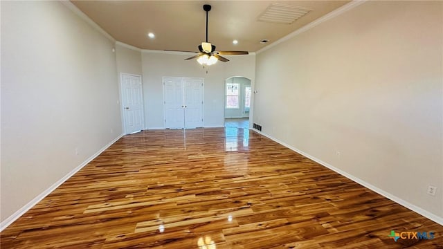 spare room featuring arched walkways, wood finished floors, visible vents, baseboards, and ornamental molding