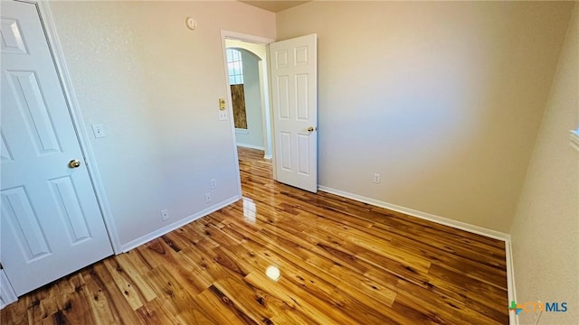 unfurnished bedroom with baseboards, arched walkways, and wood finished floors