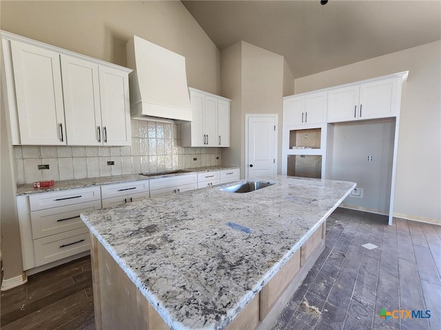 kitchen featuring white cabinets, custom exhaust hood, light stone countertops, and an island with sink