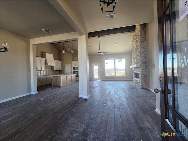 unfurnished living room with vaulted ceiling with beams, ceiling fan with notable chandelier, a stone fireplace, and dark wood-type flooring