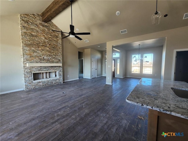 unfurnished living room with ceiling fan with notable chandelier, beam ceiling, high vaulted ceiling, a fireplace, and dark hardwood / wood-style floors