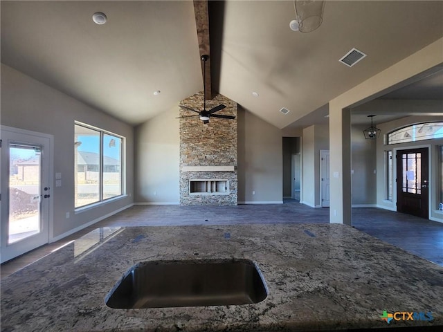 kitchen featuring ceiling fan, a fireplace, lofted ceiling with beams, and stone countertops