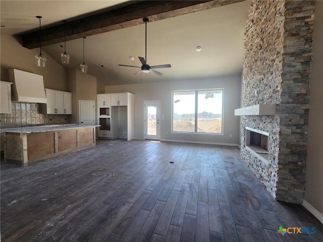 kitchen with custom range hood, ceiling fan, beamed ceiling, white cabinets, and a stone fireplace