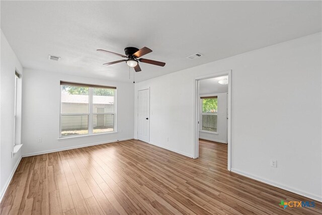empty room featuring plenty of natural light, a ceiling fan, wood finished floors, and baseboards