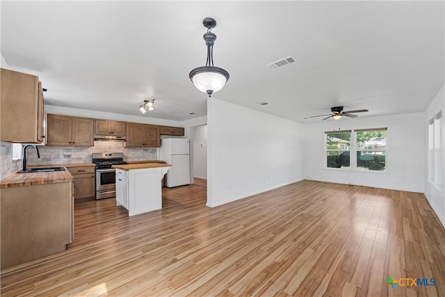 kitchen with stainless steel range with gas stovetop, freestanding refrigerator, a sink, under cabinet range hood, and open floor plan