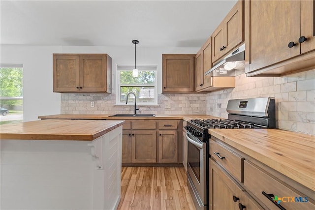kitchen with butcher block countertops, stainless steel gas range, under cabinet range hood, a sink, and light wood-style floors