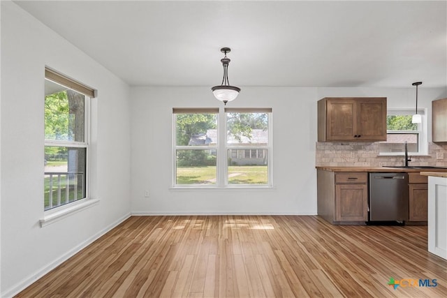 kitchen with dishwasher, a sink, light wood-style floors, decorative backsplash, and pendant lighting