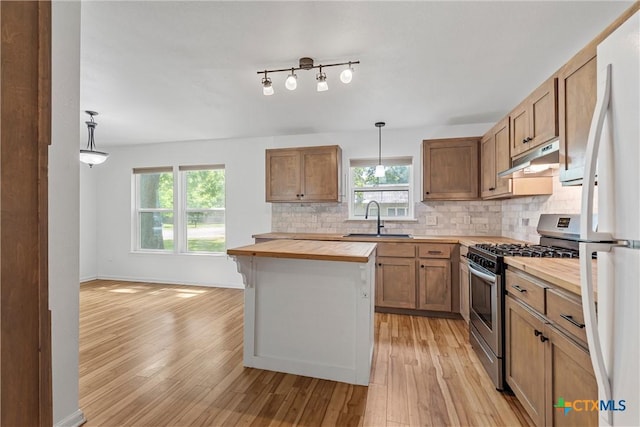 kitchen featuring butcher block counters, stainless steel range with gas cooktop, a sink, under cabinet range hood, and decorative backsplash