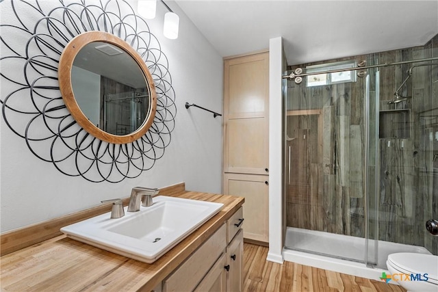 full bathroom with a stall shower, toilet, vanity, and wood finished floors