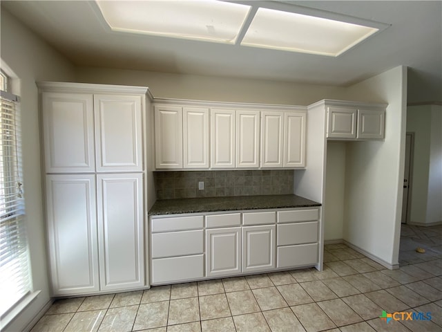 kitchen with decorative backsplash, white cabinetry, light tile patterned floors, and dark stone counters