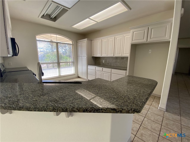 kitchen with kitchen peninsula, a kitchen breakfast bar, backsplash, light tile patterned floors, and white cabinetry