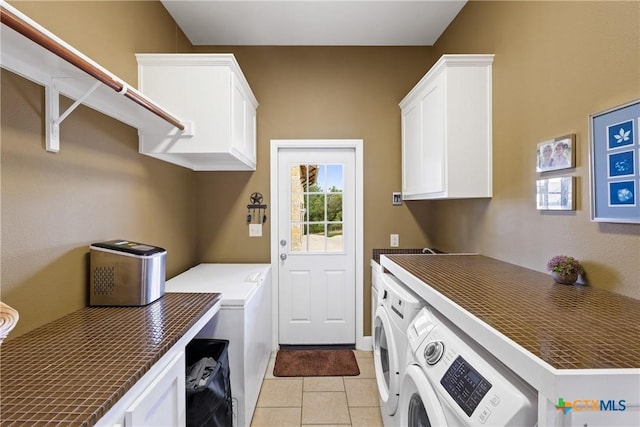 clothes washing area featuring light tile patterned floors, cabinet space, and washer and dryer