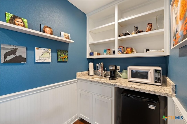 bar with a sink, a wainscoted wall, white microwave, and refrigerator
