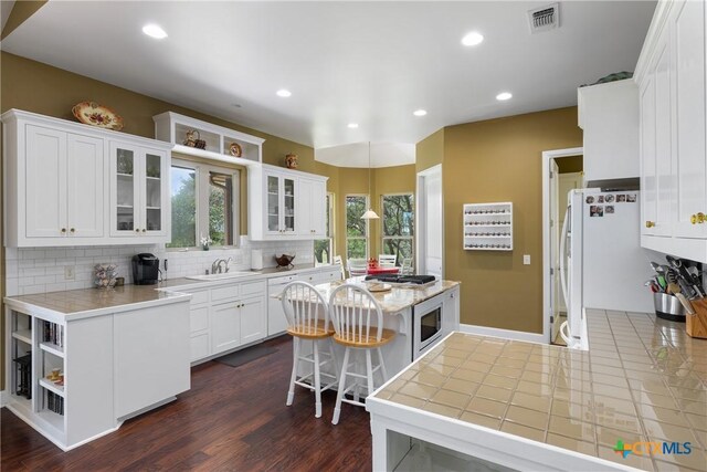 kitchen featuring visible vents, glass insert cabinets, light countertops, white cabinetry, and tasteful backsplash