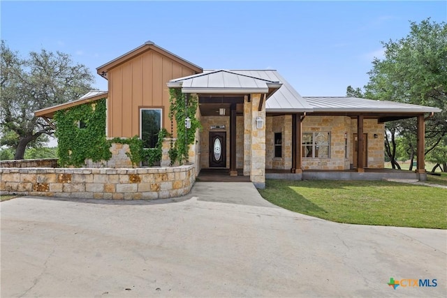 view of front facade featuring a front lawn, metal roof, stone siding, and a standing seam roof