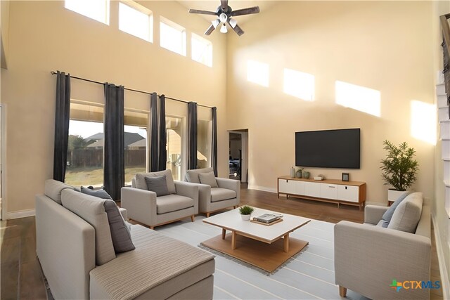 living room with dark hardwood / wood-style flooring, ceiling fan, plenty of natural light, and a towering ceiling