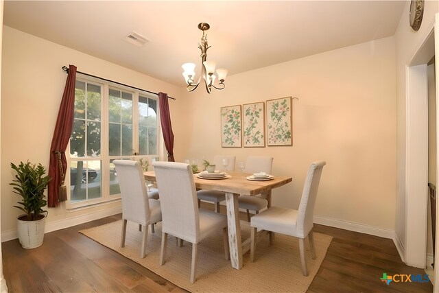 dining area with dark wood-type flooring and an inviting chandelier