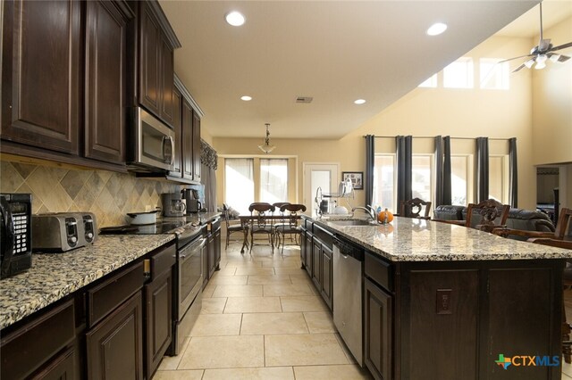 kitchen with backsplash, sink, light stone countertops, an island with sink, and appliances with stainless steel finishes