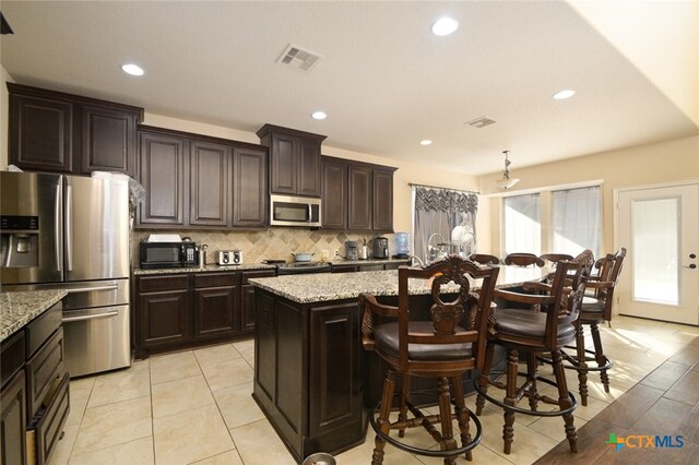 kitchen with light stone countertops, dark brown cabinets, a center island, and stainless steel appliances