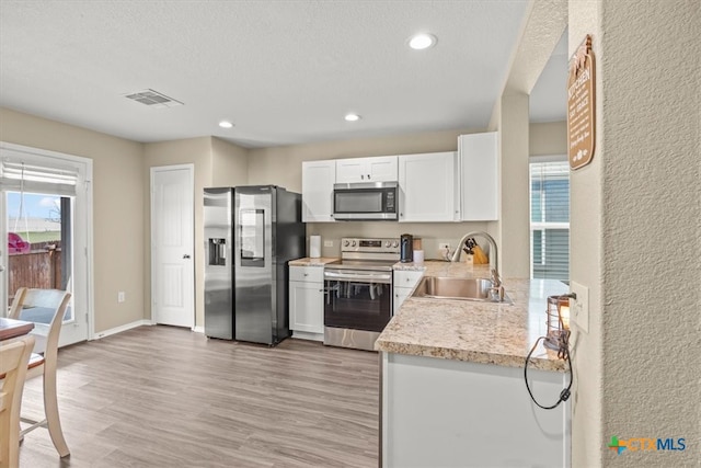 kitchen with light wood-type flooring, appliances with stainless steel finishes, a textured ceiling, sink, and white cabinets