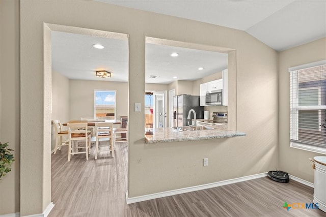 kitchen with appliances with stainless steel finishes, light hardwood / wood-style floors, white cabinets, and light stone countertops