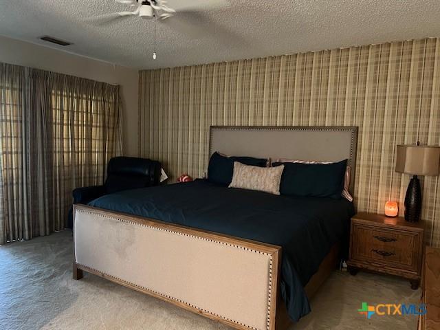 6014 Country Club Dr, Victoria, TX 77904 - bedroom featuring a ceiling fan, a textured ceiling, visible vents, carpet floors, and wallpapered walls