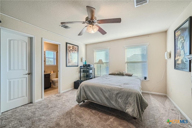 carpeted bedroom with a textured ceiling, connected bathroom, multiple windows, and ceiling fan