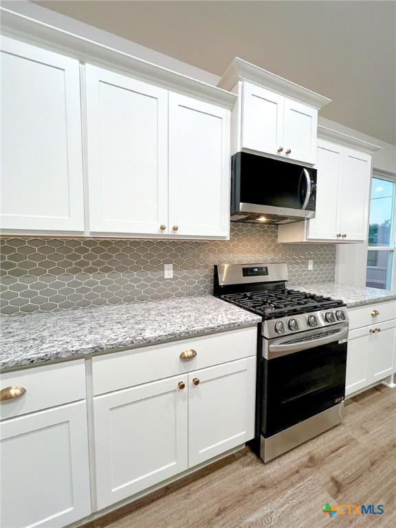 kitchen with light stone countertops, appliances with stainless steel finishes, tasteful backsplash, light hardwood / wood-style floors, and white cabinetry