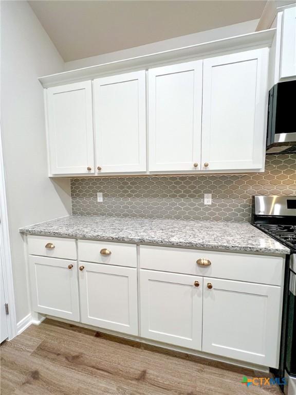 kitchen with decorative backsplash, light wood-type flooring, light stone counters, stainless steel appliances, and white cabinetry