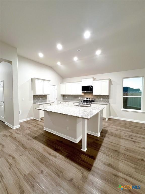 kitchen with white cabinets, vaulted ceiling, dark hardwood / wood-style floors, light stone countertops, and appliances with stainless steel finishes