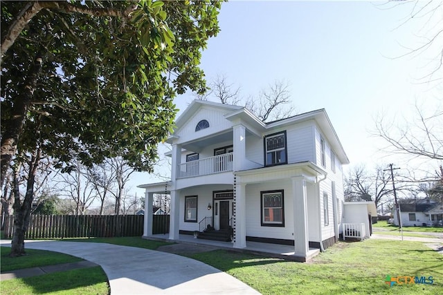 greek revival inspired property featuring a front yard, covered porch, fence, and a balcony