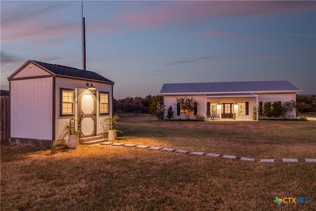 outdoor structure at dusk featuring a lawn and covered porch