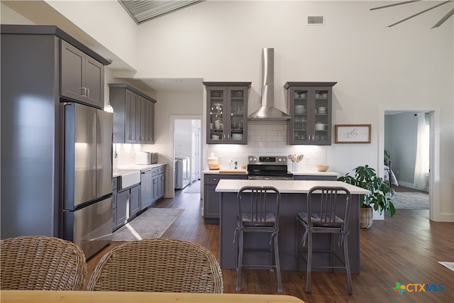 kitchen with dark wood-type flooring, a center island, gray cabinetry, wall chimney range hood, and appliances with stainless steel finishes