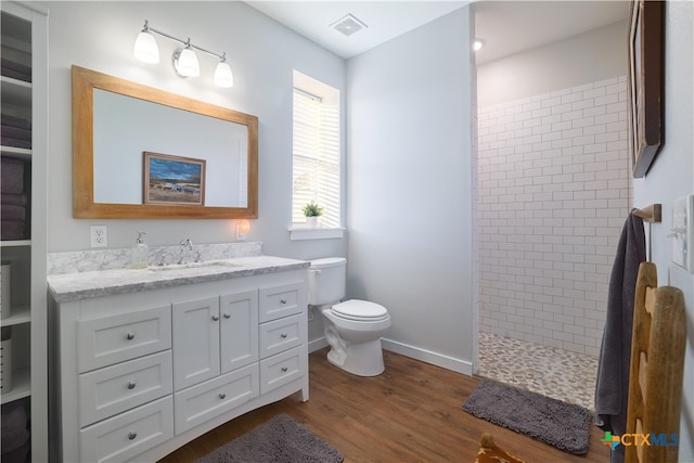 bathroom featuring toilet, vanity, hardwood / wood-style flooring, and a tile shower