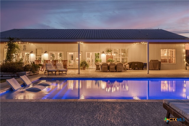 pool at dusk featuring a patio and grilling area