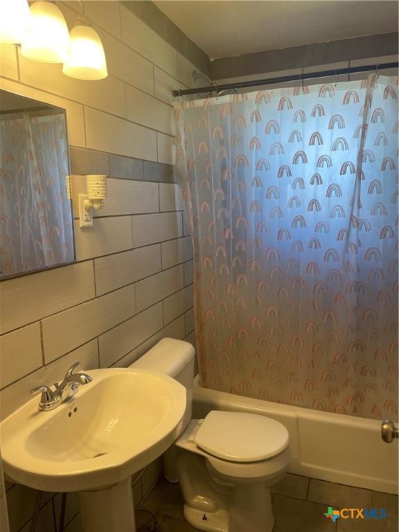 full bathroom with shower / bathtub combination with curtain, sink, tile walls, tile patterned flooring, and toilet