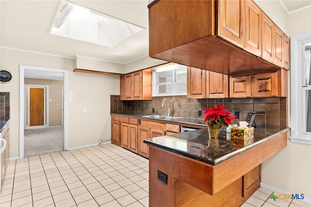 kitchen featuring kitchen peninsula, a skylight, tasteful backsplash, sink, and light tile patterned floors