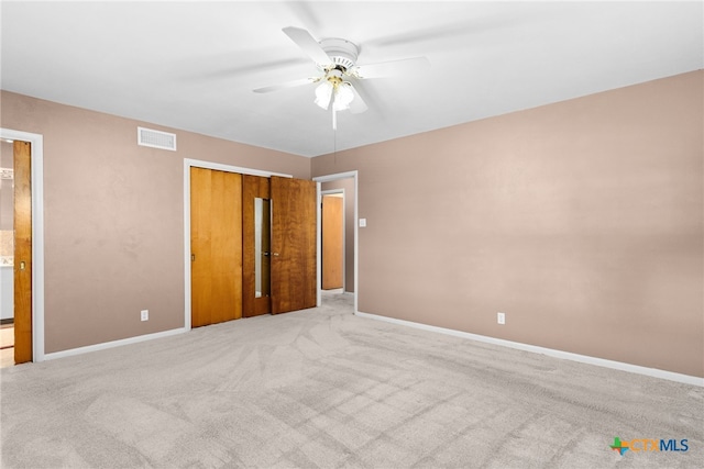 unfurnished bedroom with ensuite bath, ceiling fan, a closet, and light colored carpet