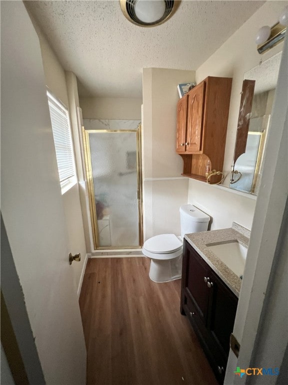 bathroom featuring toilet, a shower with door, a textured ceiling, hardwood / wood-style flooring, and vanity