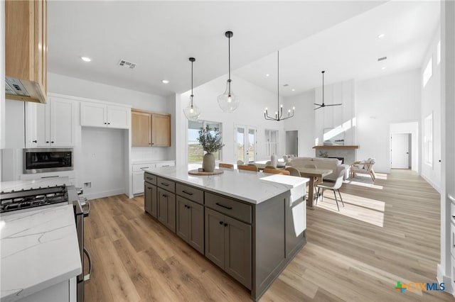 kitchen with white cabinets, light stone countertops, hanging light fixtures, and stainless steel gas range